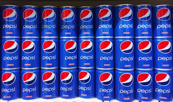 Rows of blue Pepsi cans are neatly stacked, displaying the distinctive red, white, and blue logo prominently on each can.