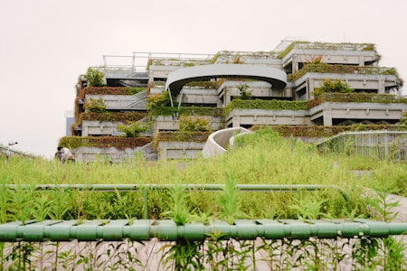 A multi-level structure covered in green plants and grass, with a modern and urban design. The foreground has lush vegetation, and there are pathways leading up to the building, creating a harmonious blend with nature.
