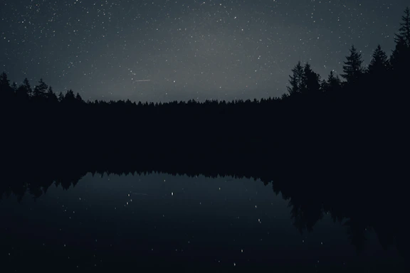 A serene moonlit night sky over a calm lake reflecting soft silver and muted indigo hues.