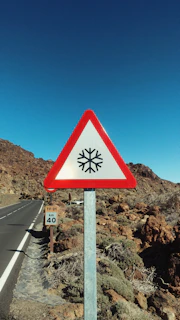 Bright yellow triangular warning sign showing a slippery road symbol.