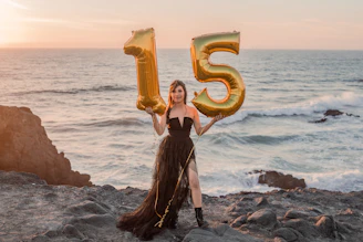a woman holding a number five balloon in front of the ocean