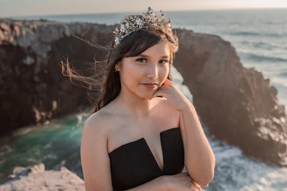 a woman wearing a tiara standing on a cliff by the ocean
