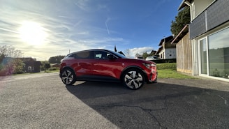 A shiny red family sedan parked outside a suburban home under a bright sky.
