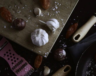 A sleek stainless steel garlic press resting on a wooden cutting board with fresh garlic cloves nearby.