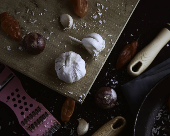 A sleek stainless steel garlic press resting on a wooden cutting board with fresh garlic cloves nearby.