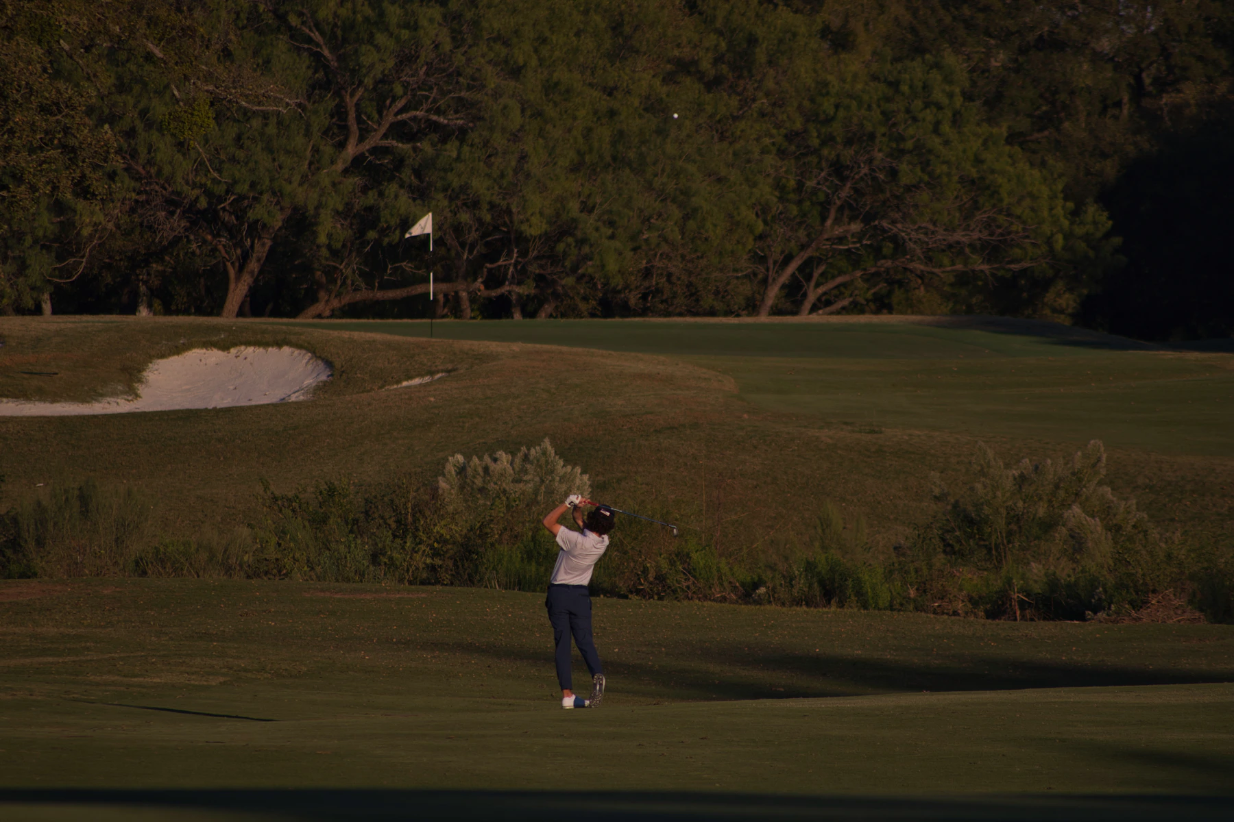 Golfer completing a full swing in evening light