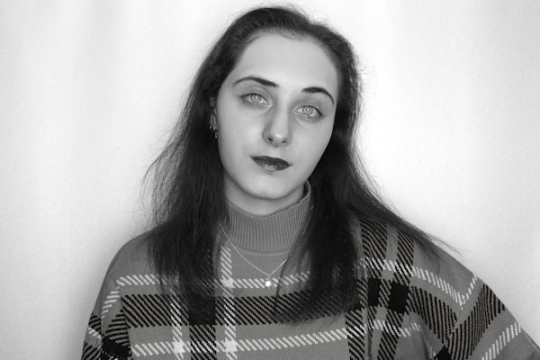 A person with light-colored eyes and dark hair is wearing a plaid sweater. The image has a monochrome effect with only the sweater in green tones.