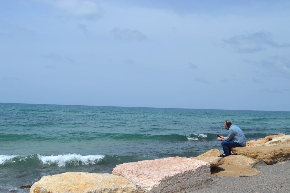 a man sitting on a rock next to the ocean