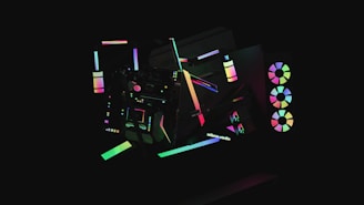 A dark background highlights various abstract geometric shapes illuminated by neon colors. The shapes include circles, rectangles, and lines that create a sense of movement and modernity. Some elements resemble computer hardware with RGB lights, giving a futuristic aesthetic.