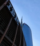 Tall skyscrapers with modern architectural design are seen against a clear blue sky, featuring glass facades. Prominent logos of large corporations appear on the buildings.