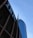 Tall skyscrapers with modern architectural design are seen against a clear blue sky, featuring glass facades. Prominent logos of large corporations appear on the buildings.