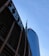 Tall skyscrapers with modern architectural design are seen against a clear blue sky, featuring glass facades. Prominent logos of large corporations appear on the buildings.