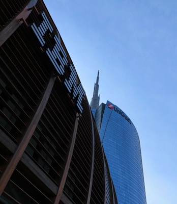 Tall skyscrapers with modern architectural design are seen against a clear blue sky, featuring glass facades. Prominent logos of large corporations appear on the buildings.