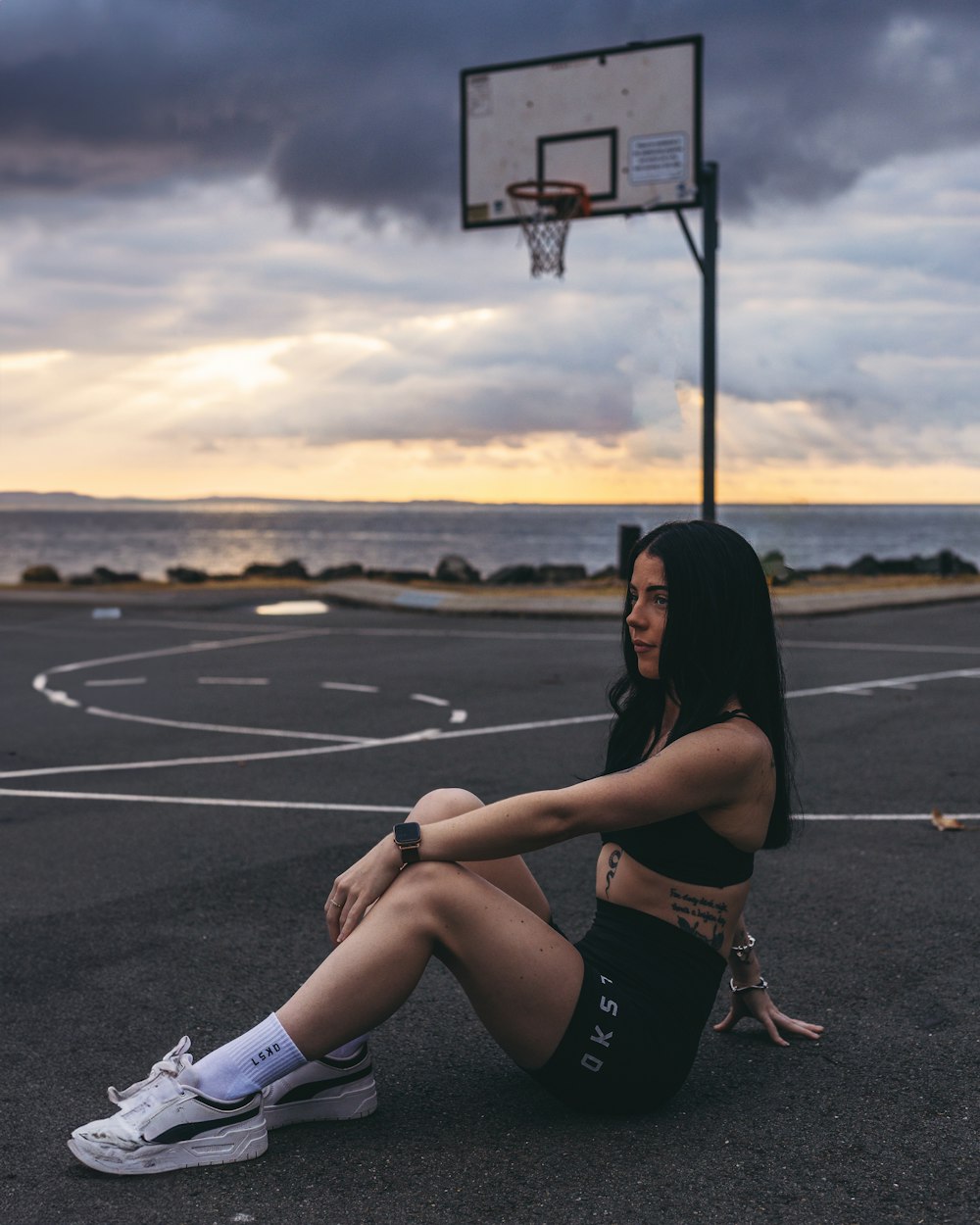 a woman sitting on the ground in front of a basketball hoop