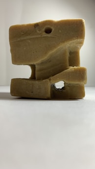A carved beige stone sculpture with various geometric shapes and a hole in the center, placed against a plain, light background.