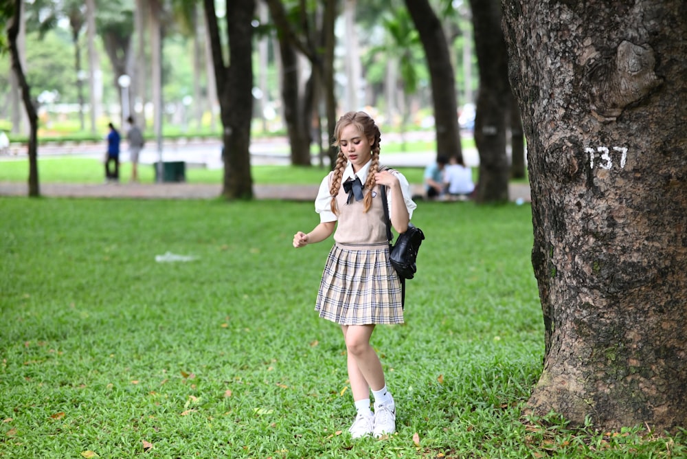 a girl in a school uniform standing next to a tree