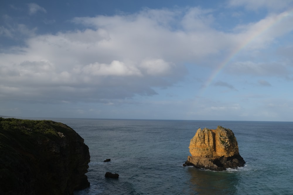 a rainbow is seen over the ocean near a rock