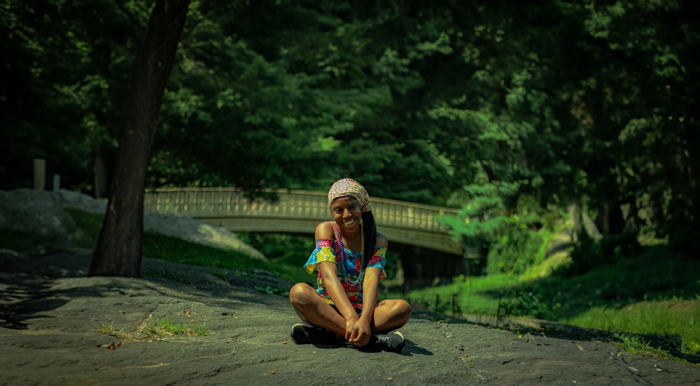 a woman sitting on the ground in front of a bridge