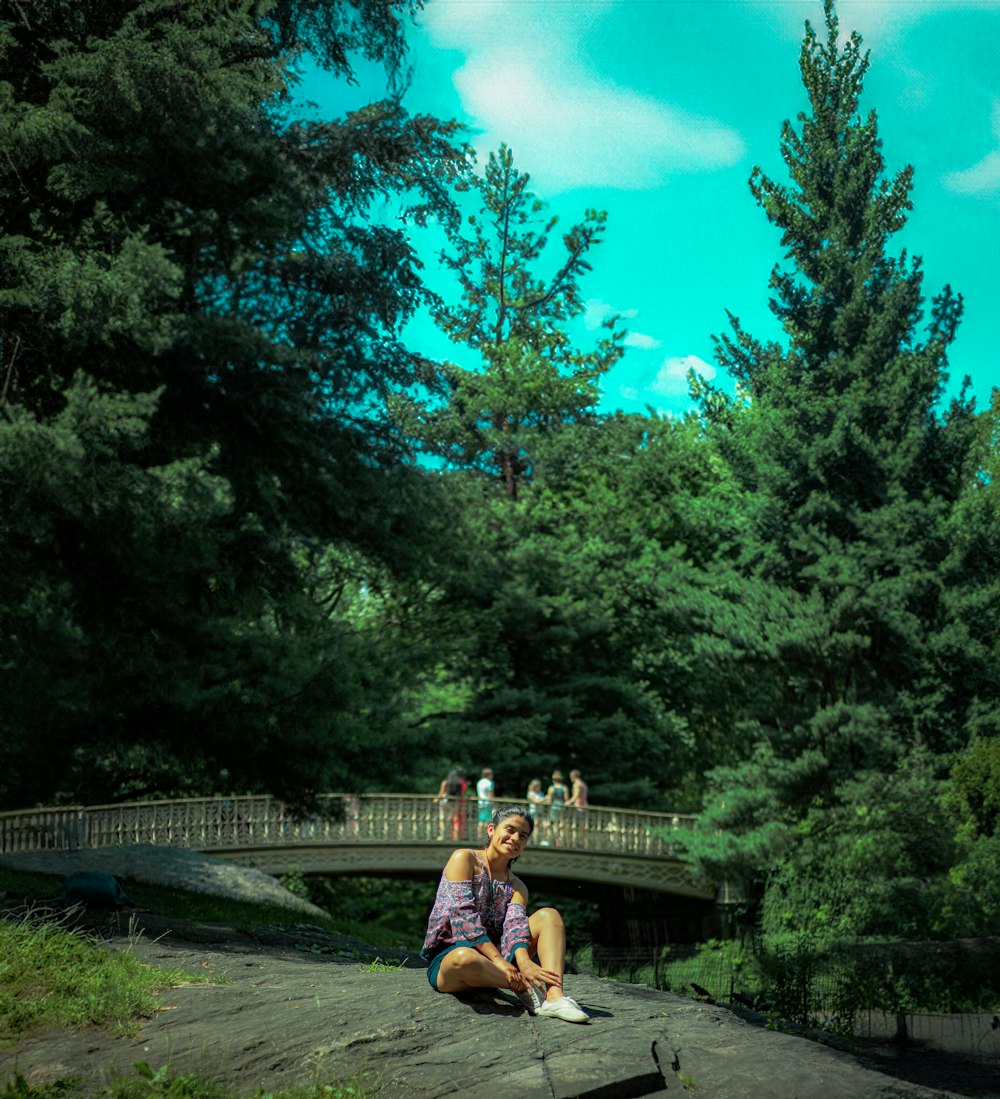 a woman sitting on a rock in front of a bridge