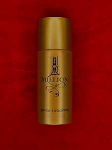 A gold cylindrical spray bottle labeled '1 Million' by Paco Rabanne set against a rich red background.