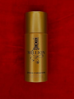 A gold cylindrical spray bottle labeled '1 Million' by Paco Rabanne set against a rich red background.