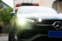 A sleek, modern car with a prominent front grille featuring a silver logo. Bright headlights are illuminated, and the car's design exudes luxury and sophistication. The background is blurred, highlighting the vehicle's details.