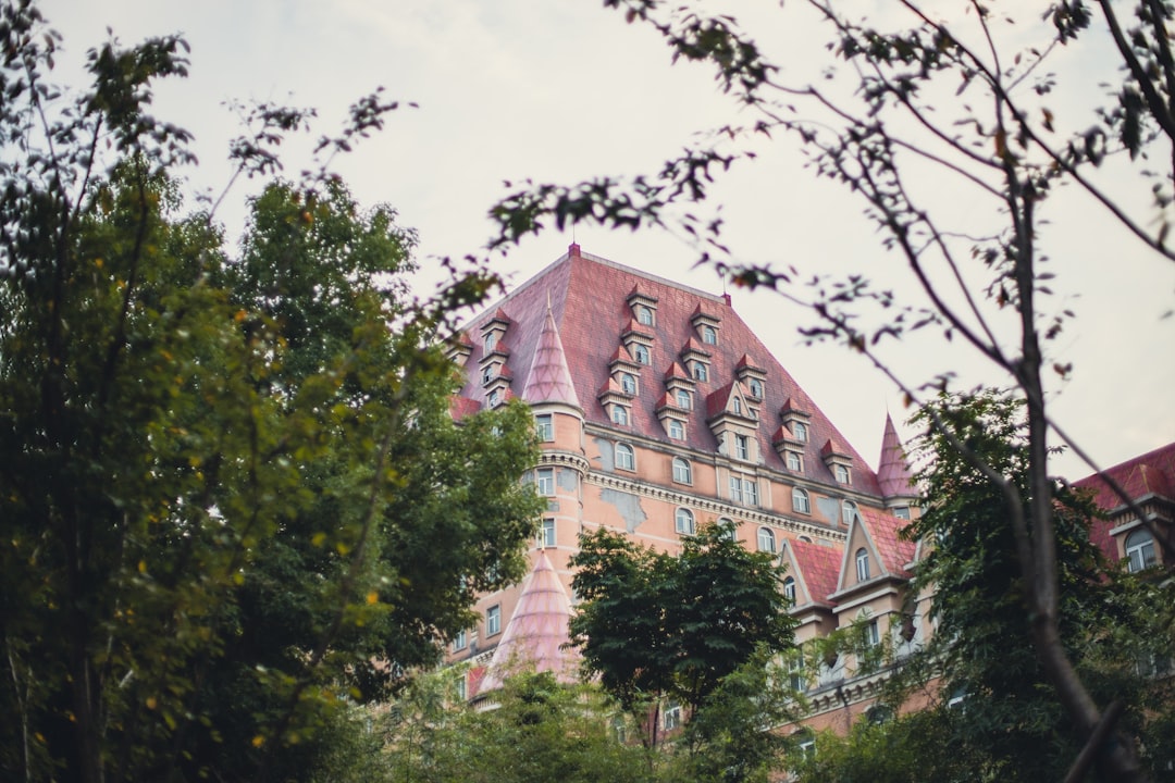 a tall building with a red roof surrounded by trees, Historic Hotel Elegance with Modern Skyline Contrast