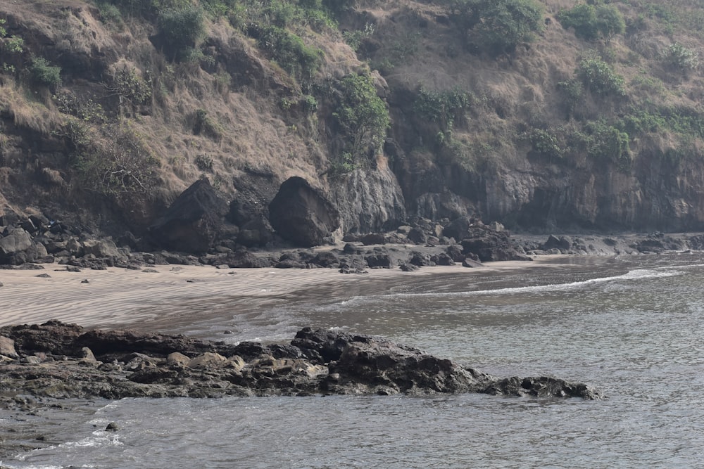 a man walking along a beach next to a cliff