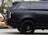 A sleek black SUV with tinted windows, featuring a modern and luxurious design. The focus is on the rear side and the distinctive alloy wheels, while the background is slightly blurred, indicating an urban setting.