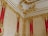 Ornate baroque-style interior decoration featuring intricate golden moldings and embellishments against rich red and cream-colored walls.