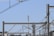 A network of power lines and metal structures is seen against a clear blue sky. In the distance, a telecommunication tower stands tall, surrounded by various wires and poles. The composition creates a geometric pattern.
