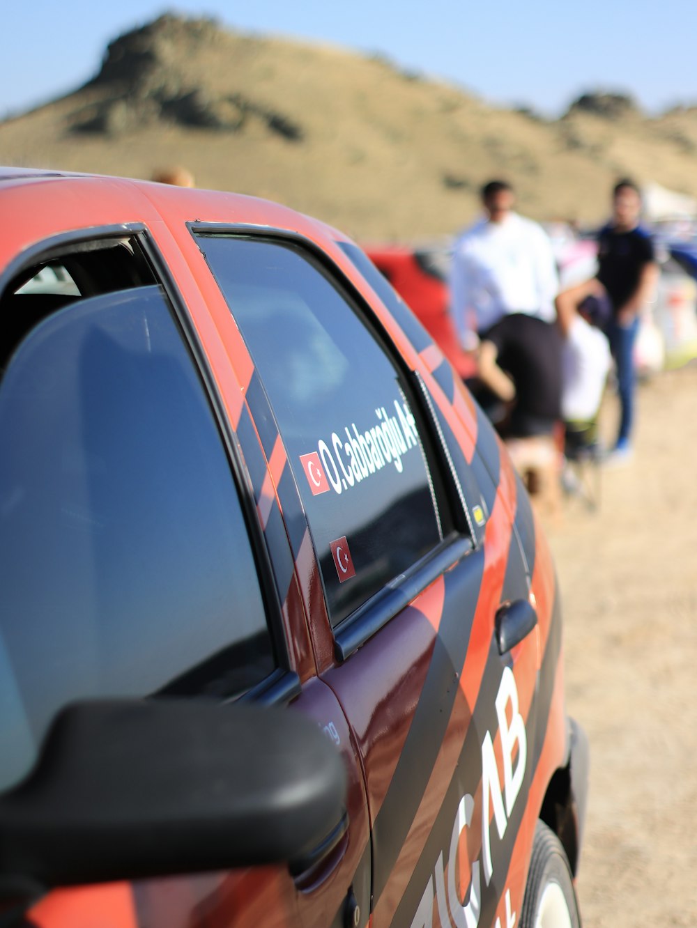 a red car parked on the side of a dirt road