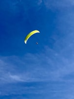 A person paragliding with a bright yellow parachute against a clear blue sky, creating a sense of freedom and adventure.