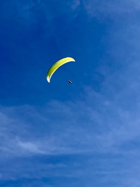 A person paragliding with a bright yellow parachute against a clear blue sky, creating a sense of freedom and adventure.