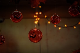 Several round ornaments with jack-o'-lantern faces hang from the ceiling, surrounded by small, glowing orange string lights. The background is dimly lit, enhancing the warm, festive glow from the lights.