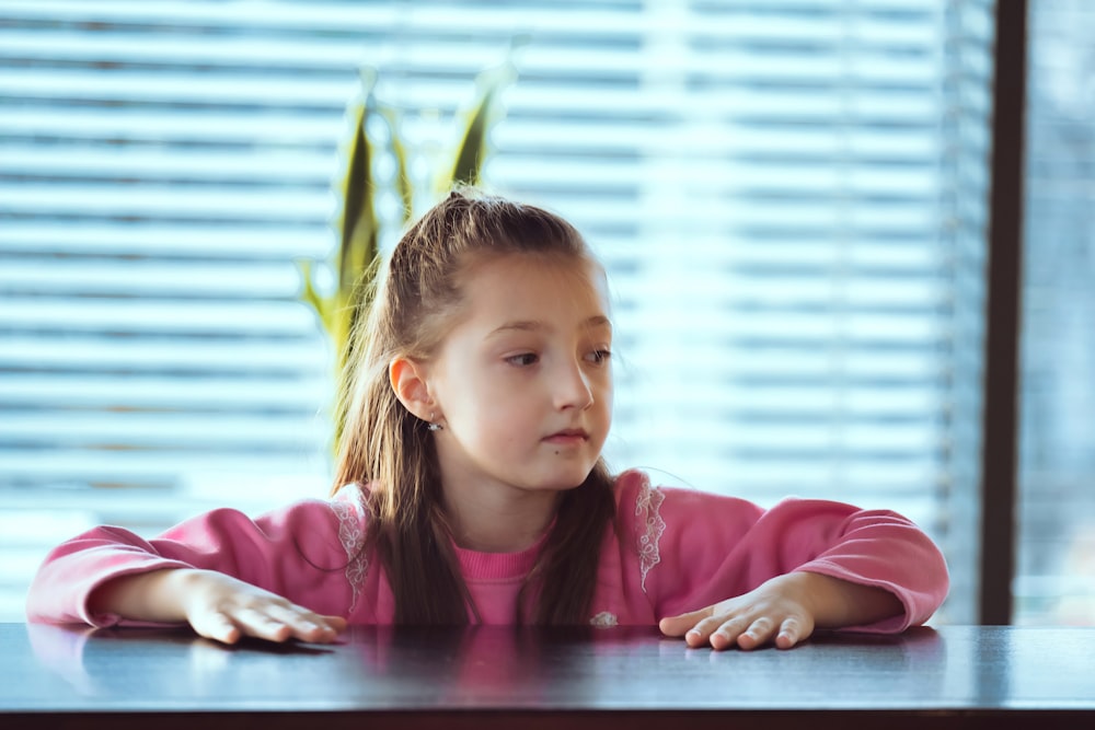 a little girl sitting at a table with her arms crossed