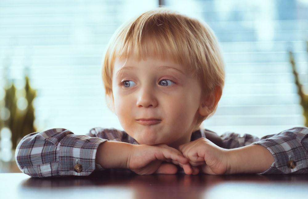 a little boy sitting at a table with his hands on his chin