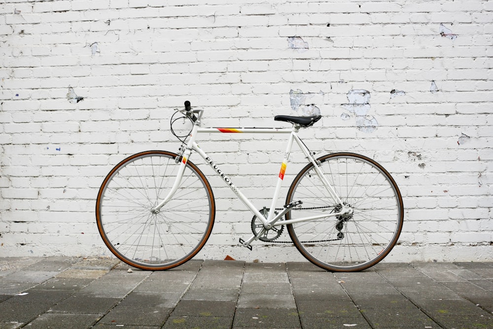 a white bicycle parked against a white brick wall