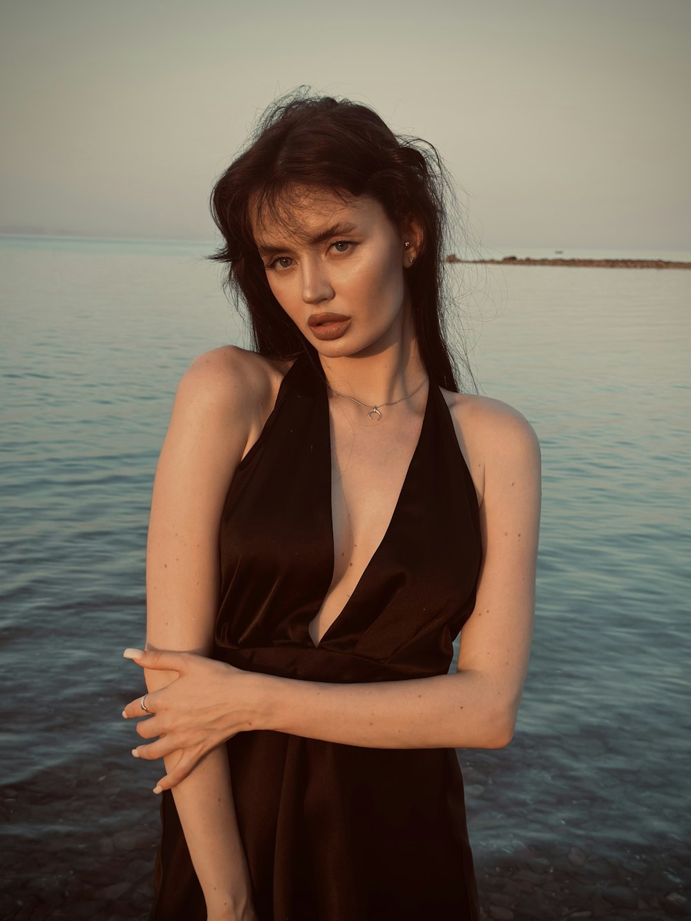 a woman in a black dress standing in front of a body of water