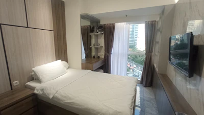 Bedroom featuring a neatly made bed, study table with lamp, and wall-mounted TV.