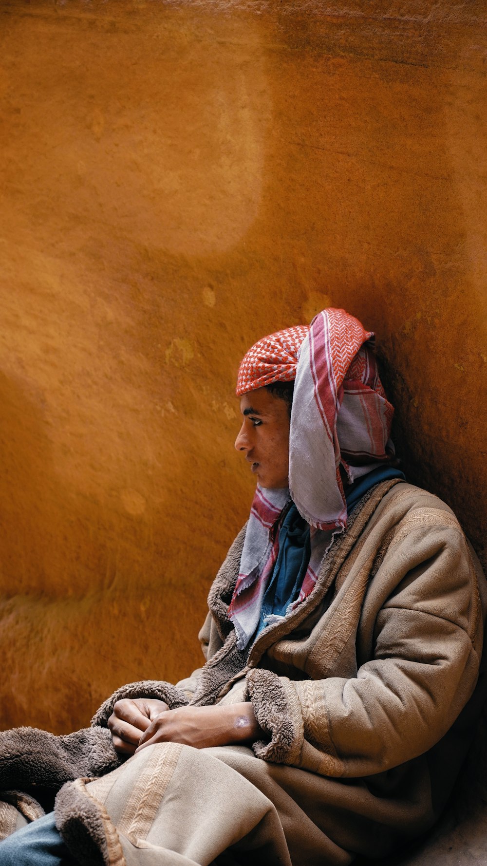 a man sitting against a wall wearing a hat