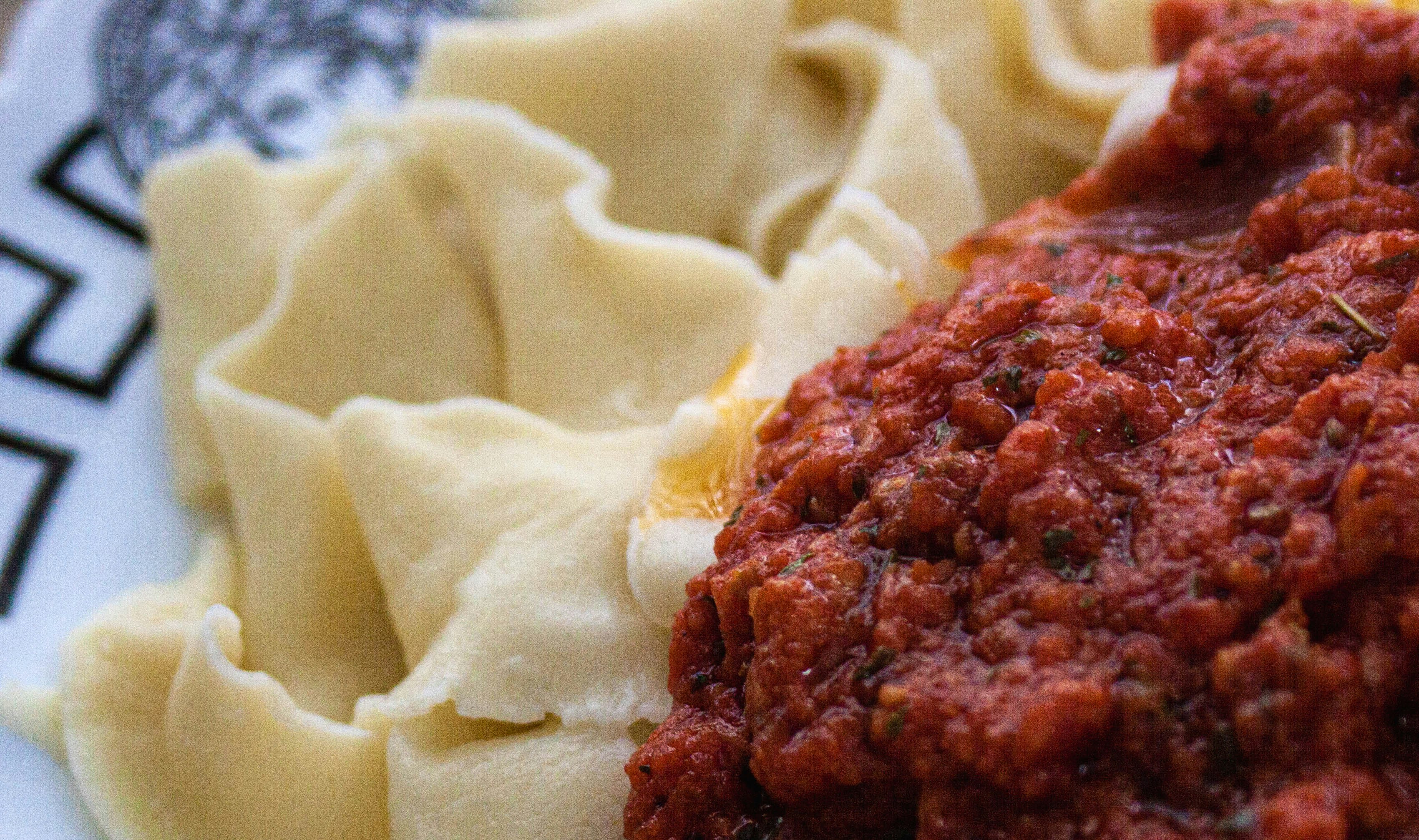 Fresh handmade pasta with rich tomato sauce in a white bowl, soft natural light, Italian kitchen setting