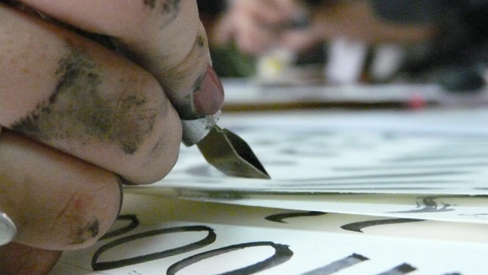 A vibrant close-up of a manga artist's hand sketching dynamic characters with ink pens.
