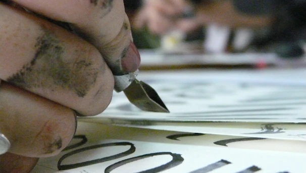 A close-up of hands carefully writing Arabic calligraphy on parchment.