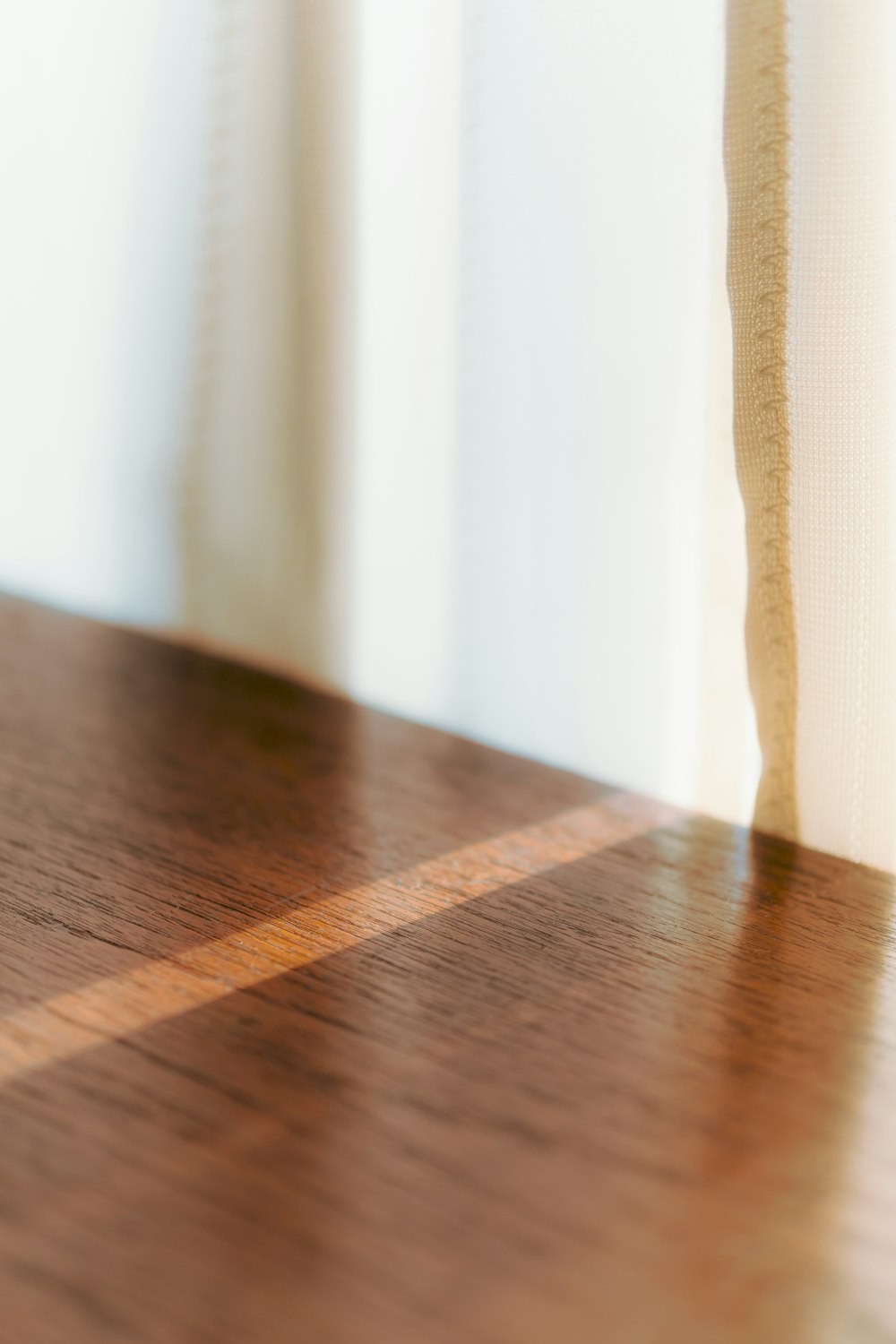 a close up of a wooden table with a white curtain in the background