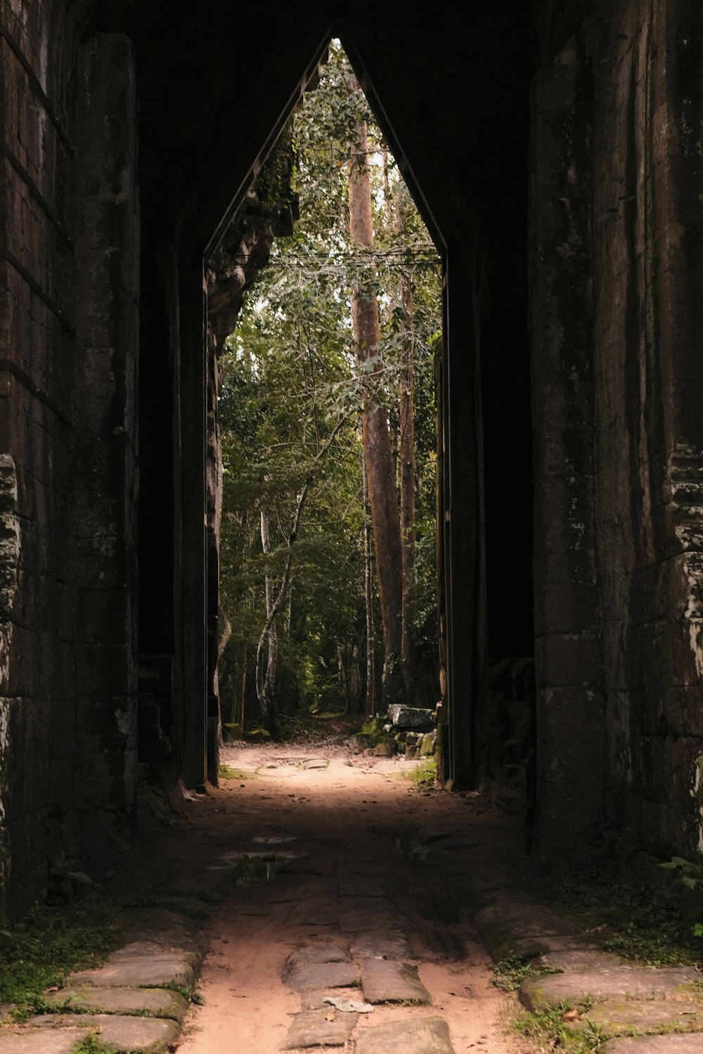 a stone archway with a dirt path leading into the woods