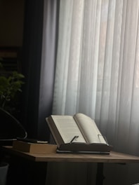 Open books and scrolls displayed on a wooden table in a serene setting.