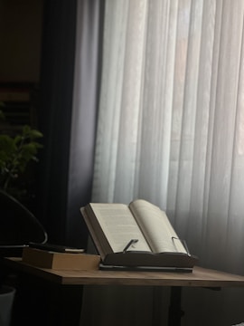 Open books and scrolls displayed on a wooden table in a serene setting.