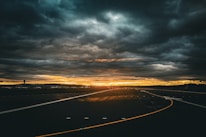 the sun is setting over a highway with dark clouds