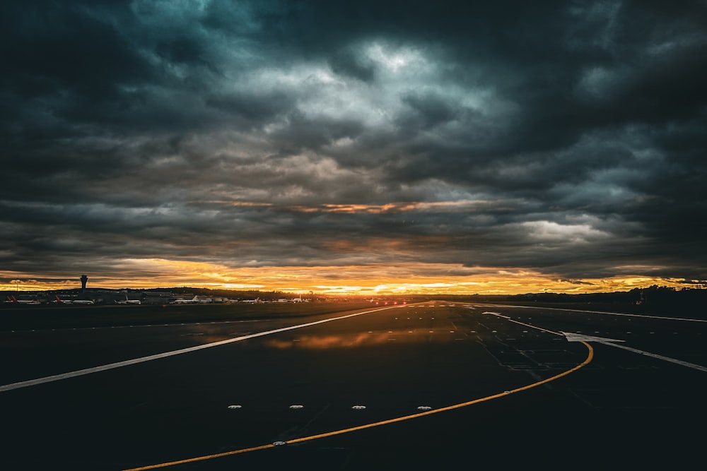 the sun is setting over a highway with dark clouds